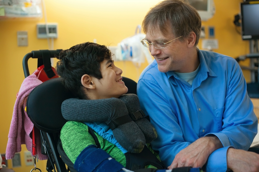 A man smiling at a young boy in a wheelchair