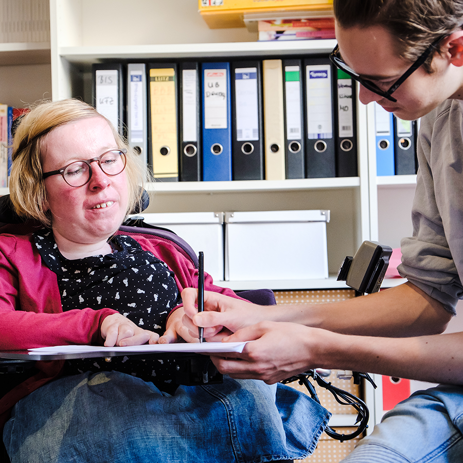 Woman in a wheelchair looking at a document being written by a man sitting next to her
