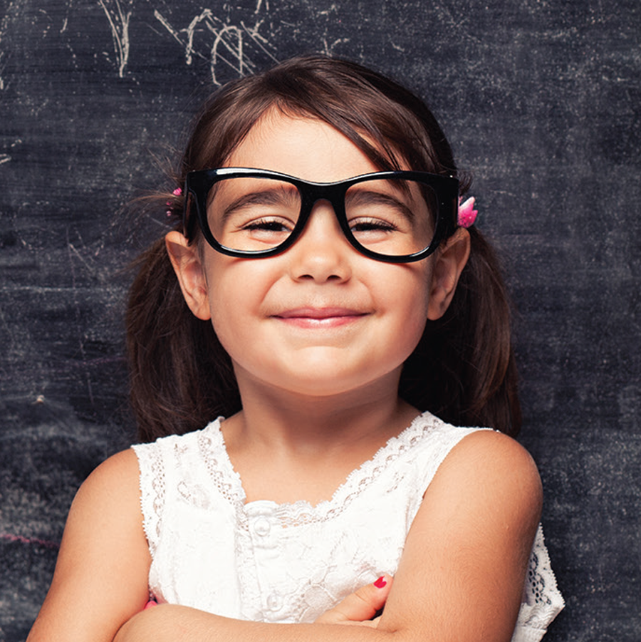 Little girl in glasses with arms crossed standing in front a chalkboard
