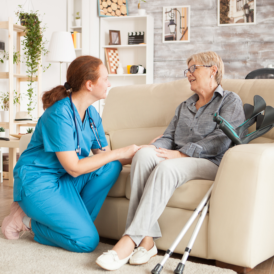 Elderly woman with crutches sitting chair with a nurse kneeling beside her