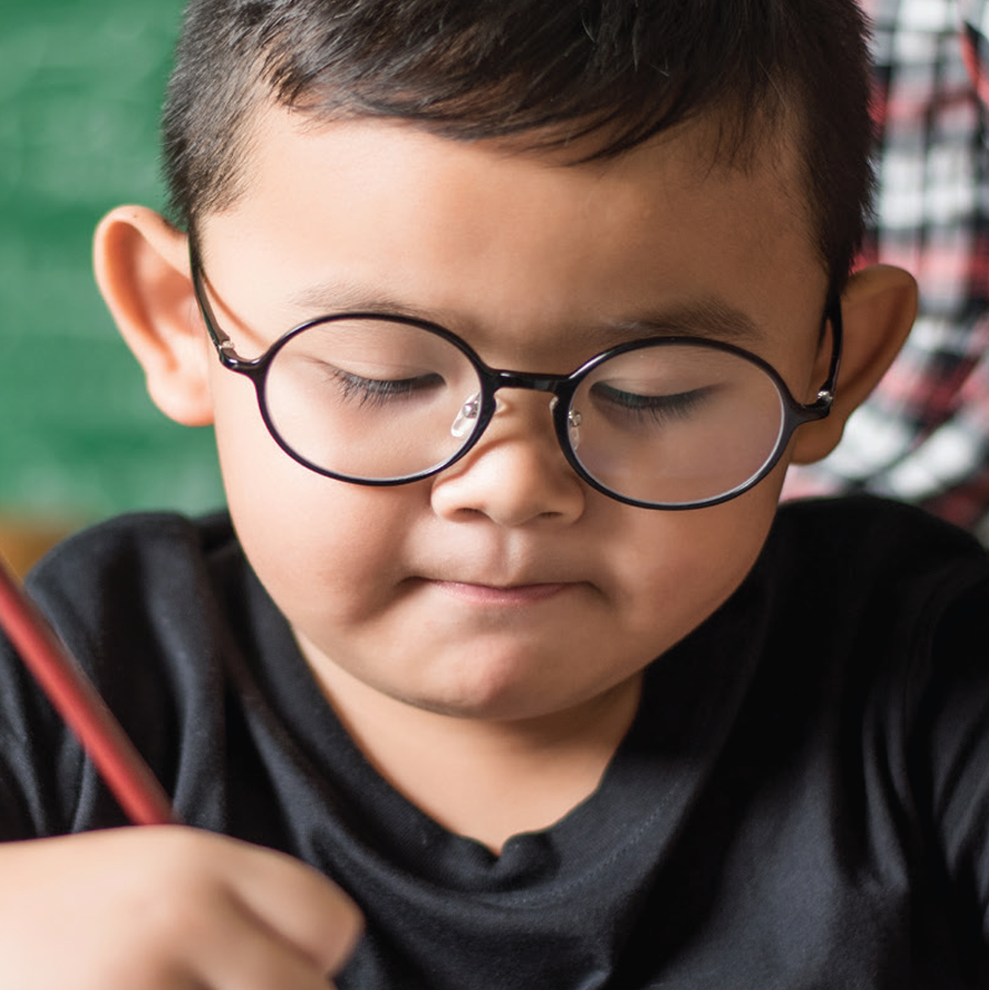 Young Asian boy in black glasses concentrating on his homework