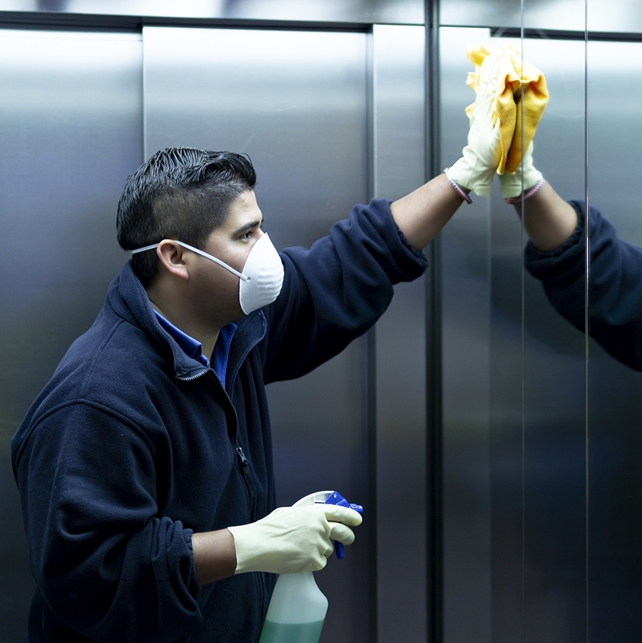 Hispanic man in jumpsuit, wearing a mask and cleaning the inside of an elevator
