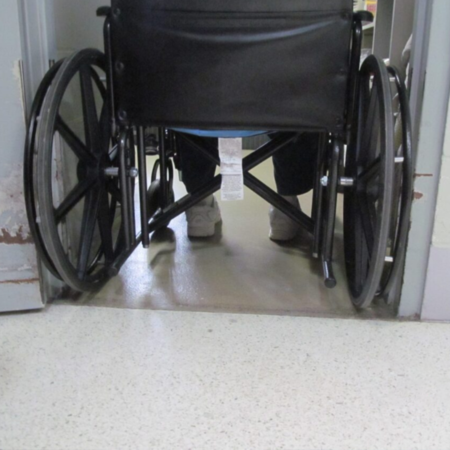 Close up of a wheelchair going through a doorway. The wheels scrape against both sides of the banged up door frame
