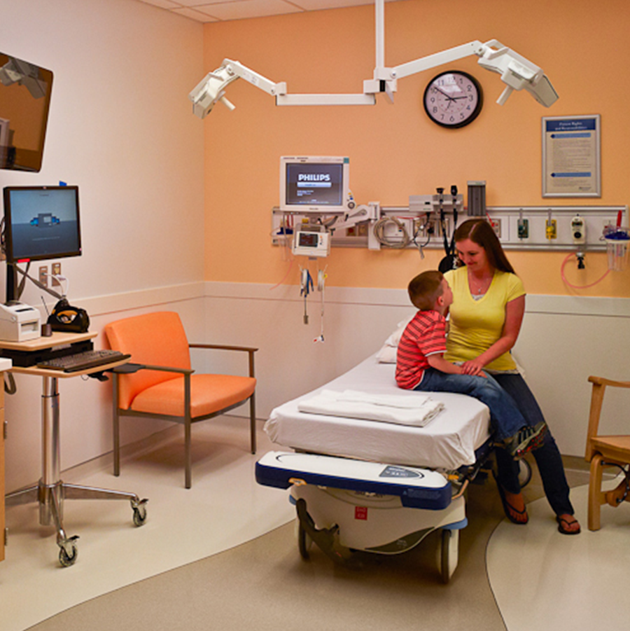 Inside of a hospital room with mother and child sitting on a hospital bed looking at each other.