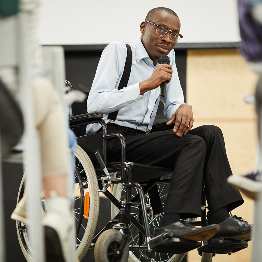 African American man in a wheelchair holding a microphone and talking to an unseen crowd of people