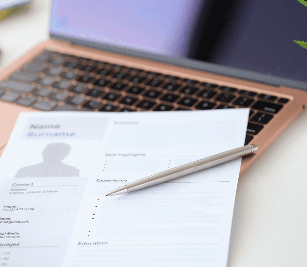 A blurry resume sits on top of a laptop's keyboard with a pen.