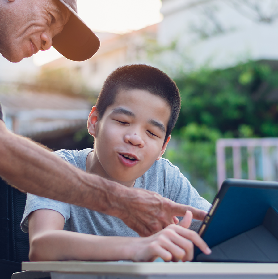 Asian boy and father sitting outside and using a tablet to communicate with each other