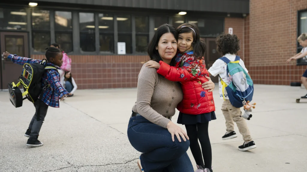 Asian American mother and daughter hug in front of a school