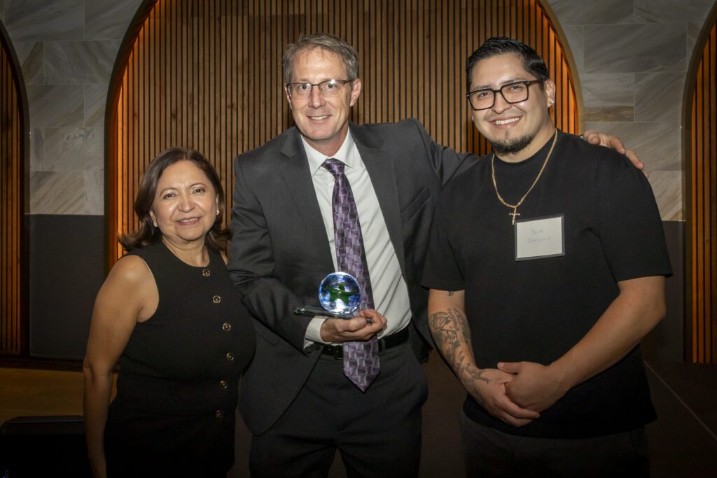 A man with an award stands with a woman and another man