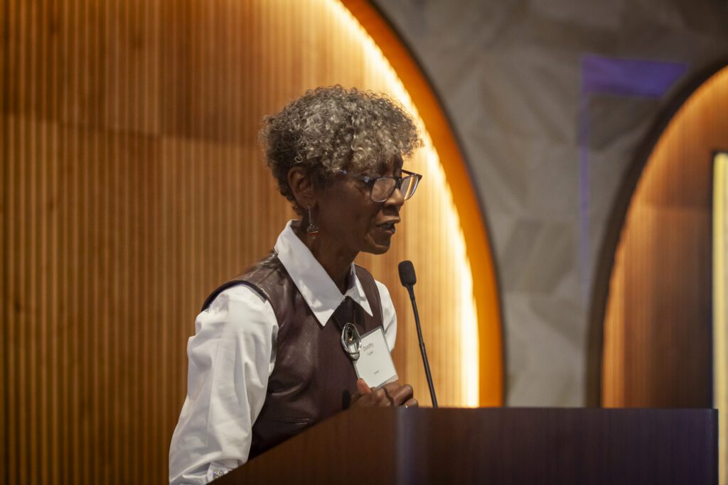 Dorothy Tucker speaking at a podium in a crowded room at the Chicago winery.
