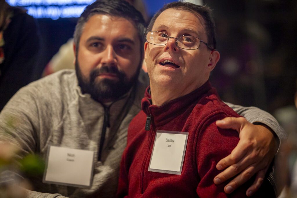 Two men sitting near each other watching the event in a crowded room at the Chicago winery.