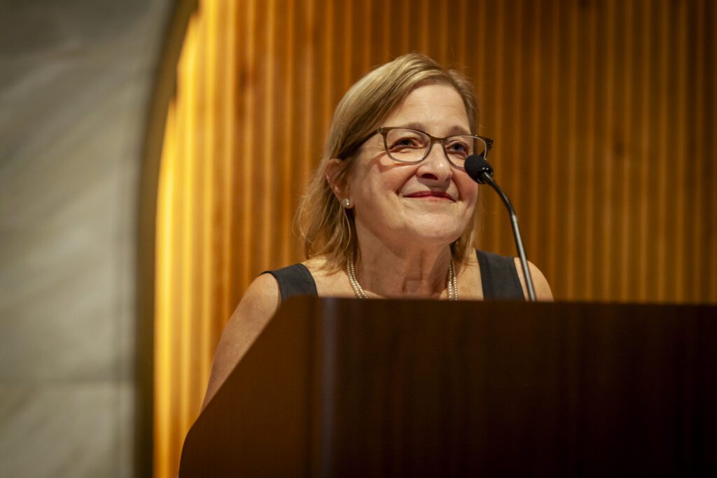 Woman speaking at a podium in a crowded room at the Chicago winery.